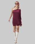 Woman wearing a burgundy one-shoulder dress and white boots on a white background