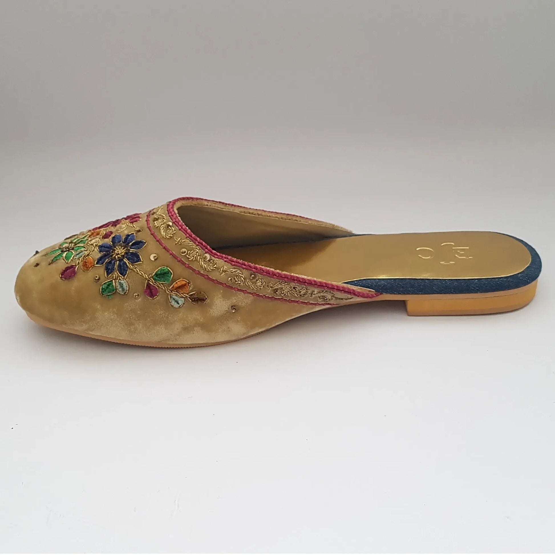 Pair of gold embroidered slippers with colorful floral designs on a light gray background