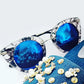 Blue sunglasses with clear frames on a blue fabric background with decorative elements.
