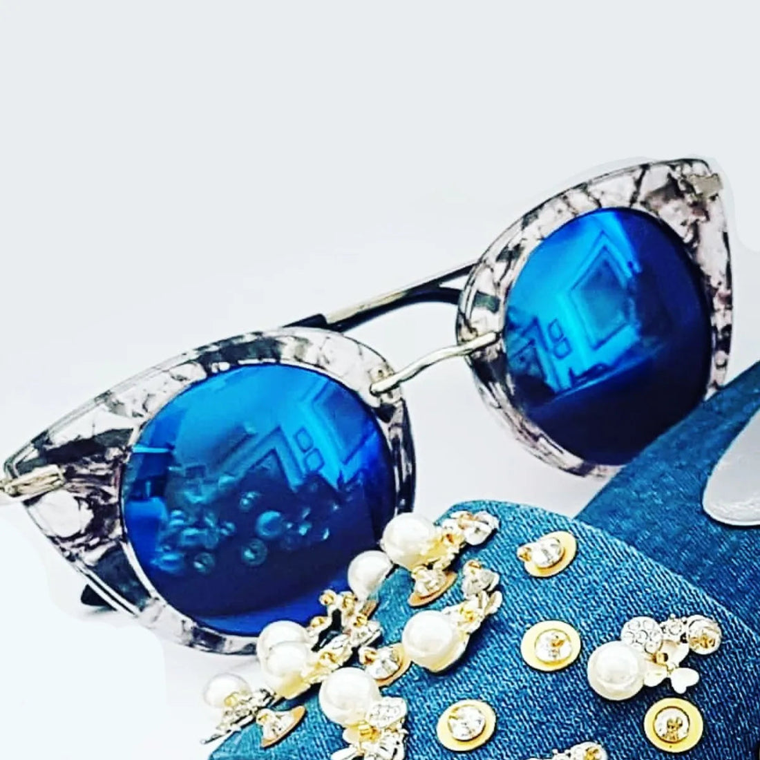 Blue sunglasses with clear frames on a blue fabric background with decorative elements.