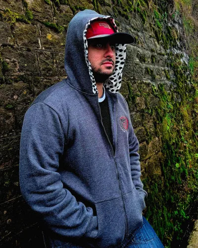 Man wearing a gray hoodie and red cap against a stone wall