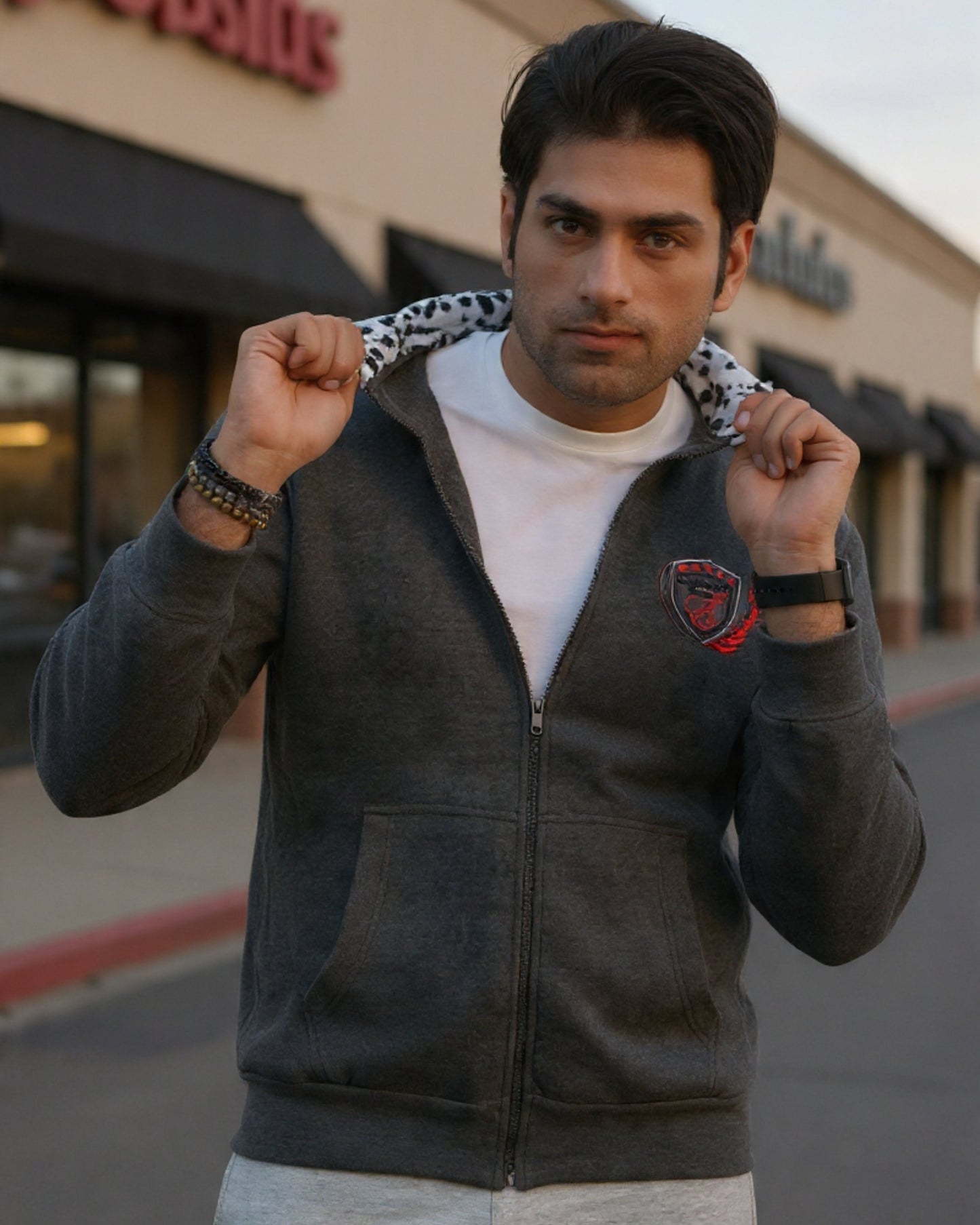 Man wearing a dark gray hoodie with a logo, standing in front of a store.