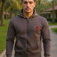 Man wearing a brown hoodie with a logo, standing outdoors with palm trees in the background