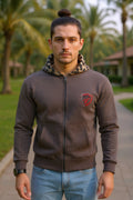 Man wearing a brown hoodie with a logo, standing outdoors with palm trees in the background