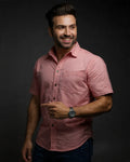 Man wearing a pink shirt and watch against a dark background