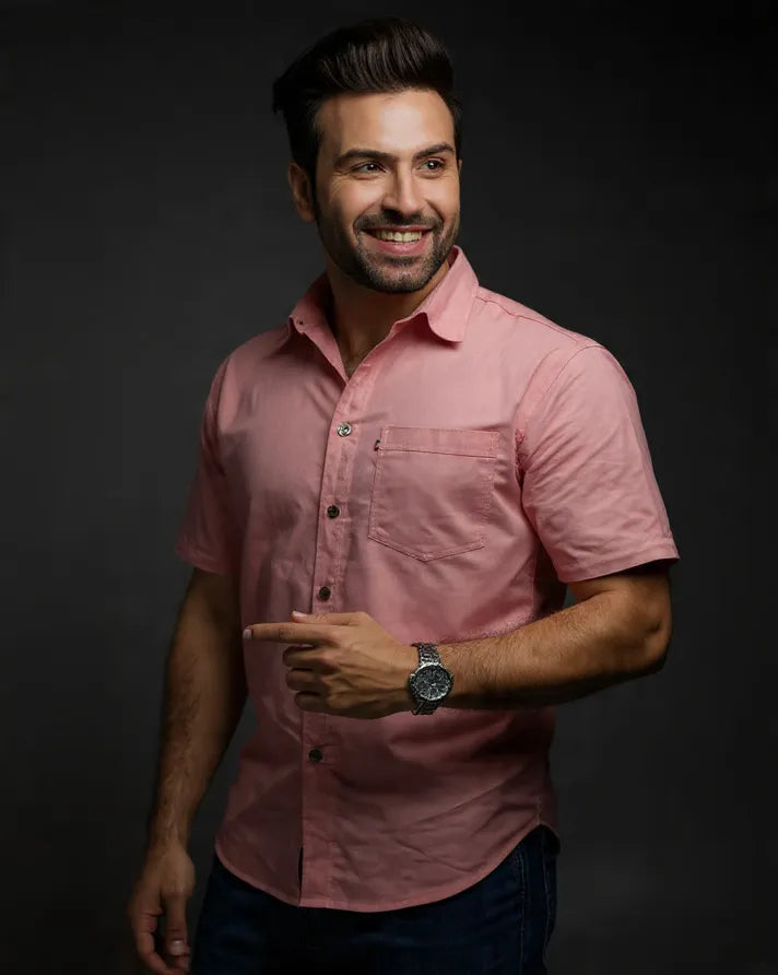 Man wearing a pink shirt and watch against a dark background