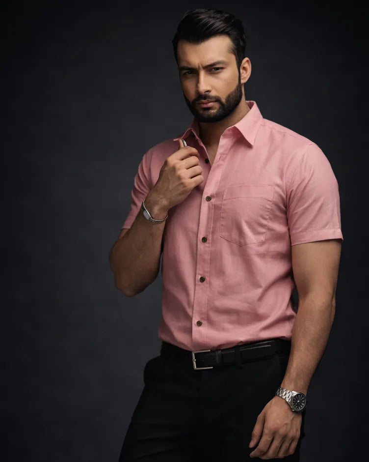 Man wearing a pink shirt and black pants sitting on a dark background
