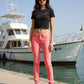 Woman wearing a black t-shirt and pink pants standing by a marina with boats in the background.