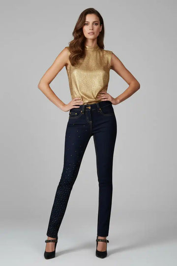 Woman wearing a gold top and dark jeans on a gray background