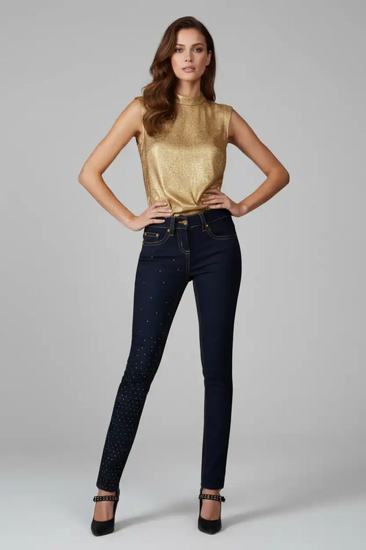 Woman wearing a gold top and dark jeans on a gray background