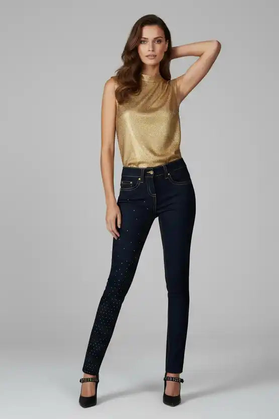Woman wearing a gold top and dark jeans on a gray background