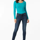 Woman wearing a teal long-sleeve top and dark blue jeans on a white background