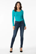 Woman wearing a teal long-sleeve top and dark blue jeans on a white background