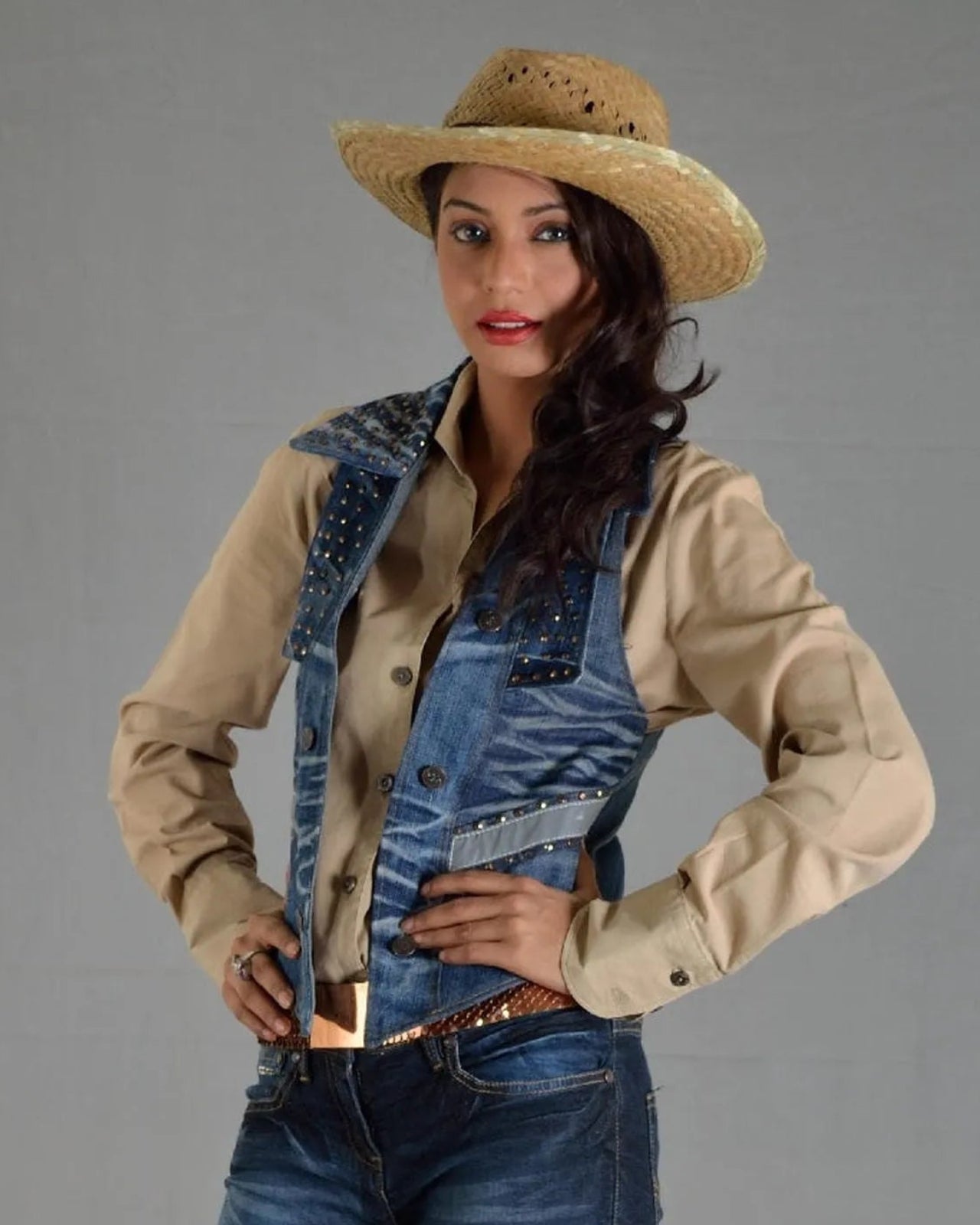 Woman wearing a beige shirt, denim overalls, and a straw hat on a gray background