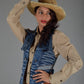 Woman wearing a cowboy hat and denim vest against a gray background