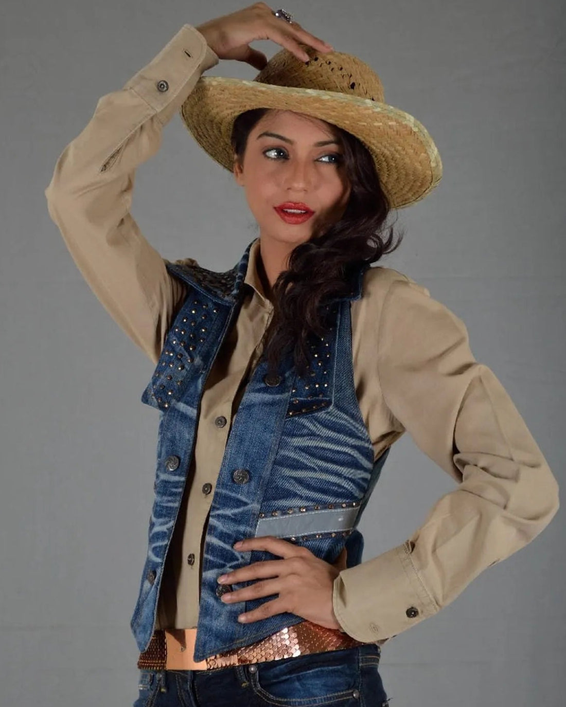 Woman wearing a cowboy hat and denim vest against a gray background