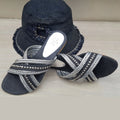 Black sandals with silver embellishments and a matching black hat on a light wooden surface.