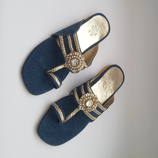 Pair of blue sandals with gold embellishments on a light gray background
