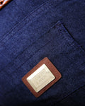 Close-up of a blue denim bag with a leather patch and brand logo.