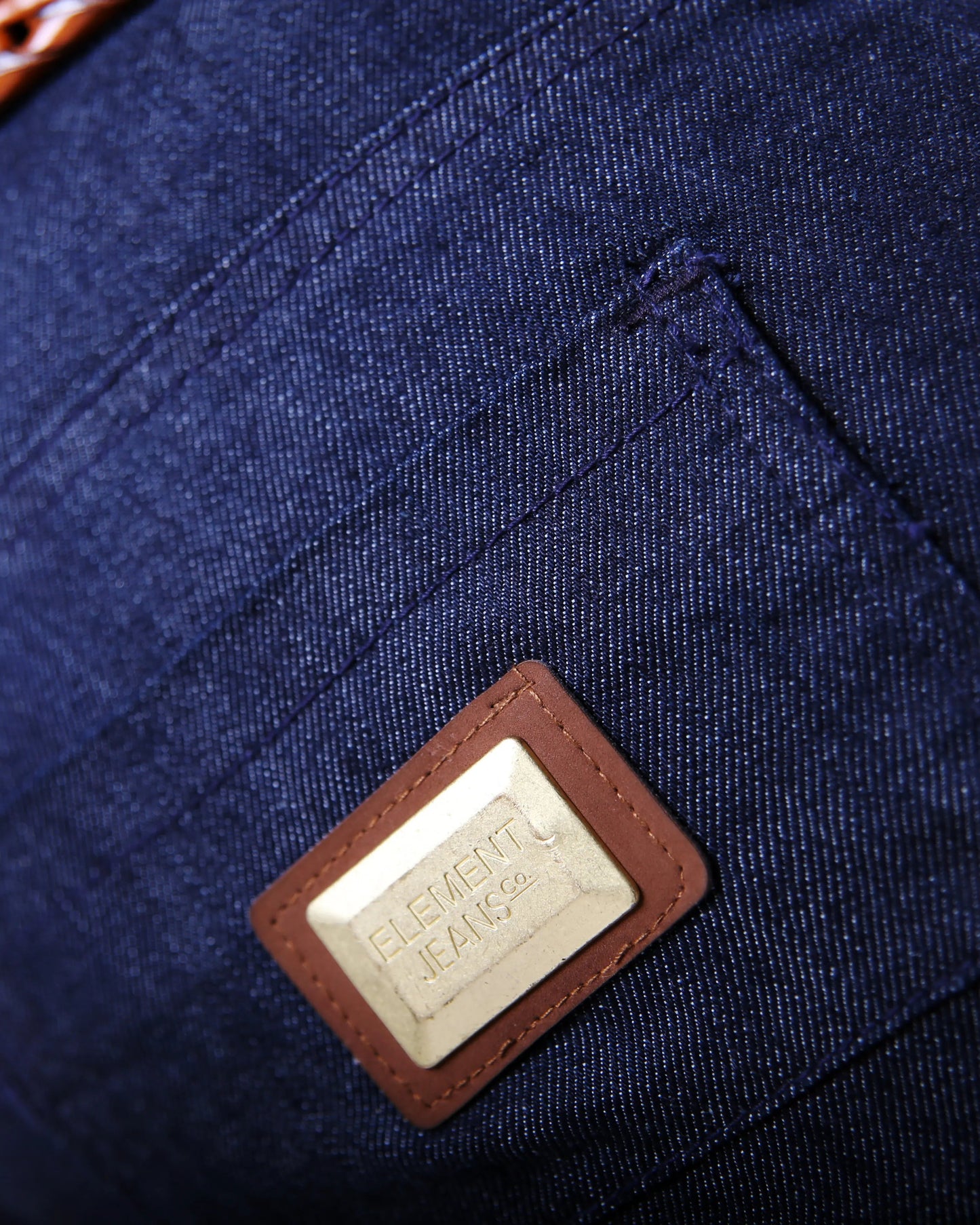 Close-up of a blue denim bag with a leather patch and brand logo.