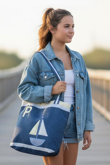 Denim tote bag with sailboat design and letter 'P' on a concrete surface