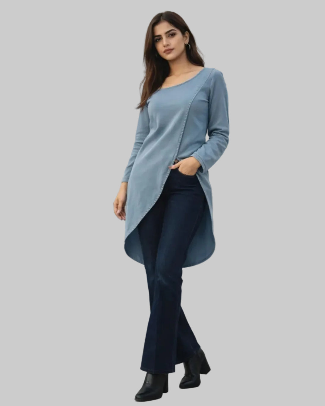 Woman wearing a denim long-sleeve top and dark pants standing in front of a cityscape window.
