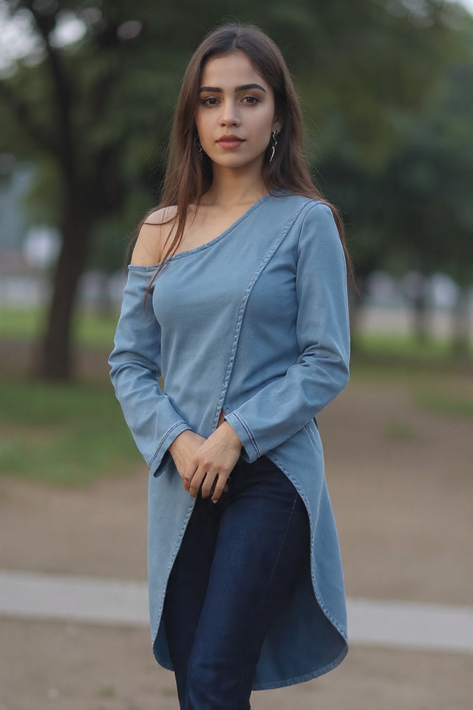 Woman wearing a blue long-sleeve top and dark jeans standing outdoors.