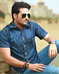 Man wearing a blue denim shirt and sunglasses sitting outdoors with a blurred background
