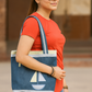 Woman holding a blue tote bag with a sailboat design, wearing a red shirt and sunglasses.