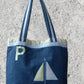 Navy tote bag with sailboat design and letter 'P' on a concrete surface