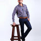 Man wearing a blue and red checkered shirt and dark jeans standing on a wooden stool against a white background