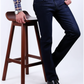 Person wearing dark jeans and a plaid shirt standing next to a wooden stool on a white background