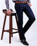 Person wearing dark jeans and a plaid shirt standing next to a wooden stool on a white background