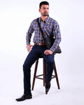 Man wearing a blue plaid shirt and dark jeans sitting on a wooden stool against a white background