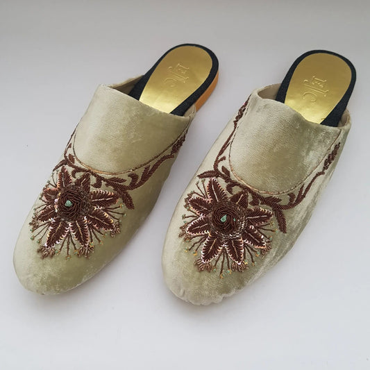 Pair of beige slippers with floral embroidery on a white background