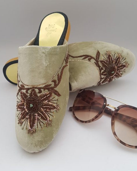A pair of fawn velvet mule shoes with brown embroidery, displayed alongside a pair of sunglasses.