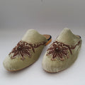 Pair of beige slippers with brown floral embroidery on a light gray background