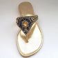 Gold sandal with decorative strap featuring blue and gold stones on a white background