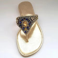 Gold sandal with decorative strap featuring blue and gold stones on a white background