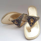Gold sandals with decorative straps featuring gemstones on a gray background