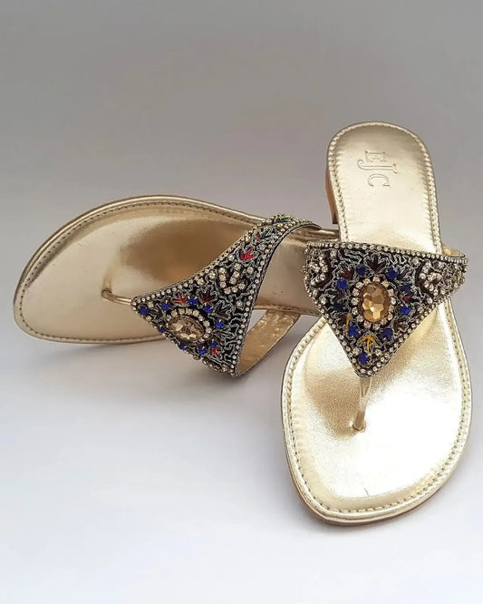 Gold sandals with decorative straps featuring gemstones on a gray background