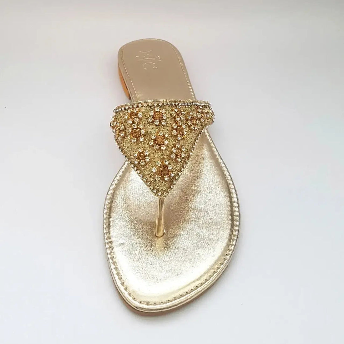 Gold sandal with embellishments on a gray background