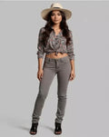 Woman wearing a patterned blouse, gray pants, and a beige hat on a gray background