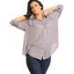 Woman wearing a gray button-up shirt and dark jeans standing against a plain wall.