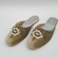 Pair of gold embellished slippers on a light gray background