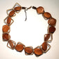 A handcrafted wooden necklace with brown beads and metallic frame links, displayed against a plain background.
