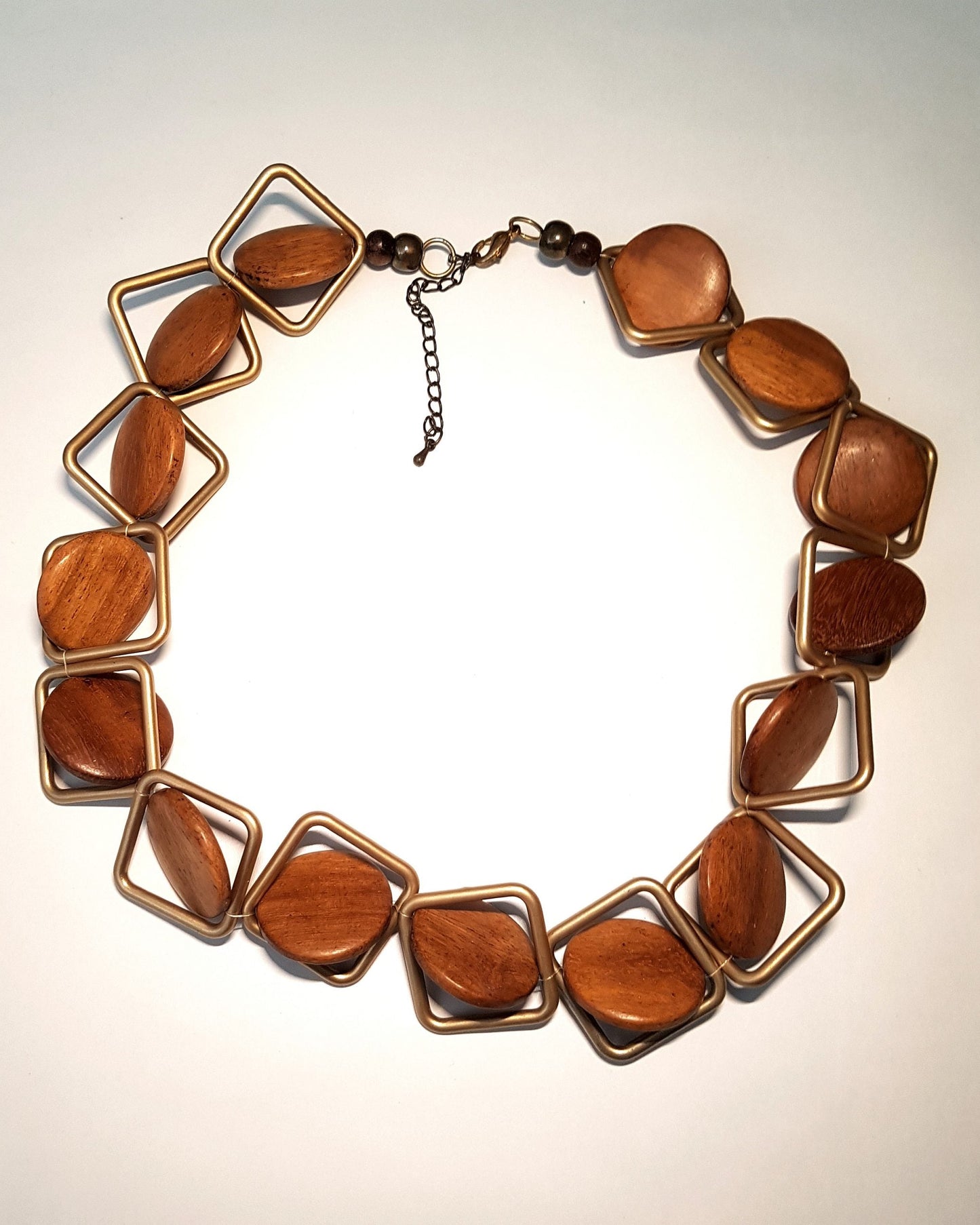 A handcrafted wooden necklace with brown beads and metallic frame links, displayed against a plain background.