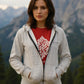 Woman wearing a gray hoodie over a red shirt with text, standing in front of mountains.
