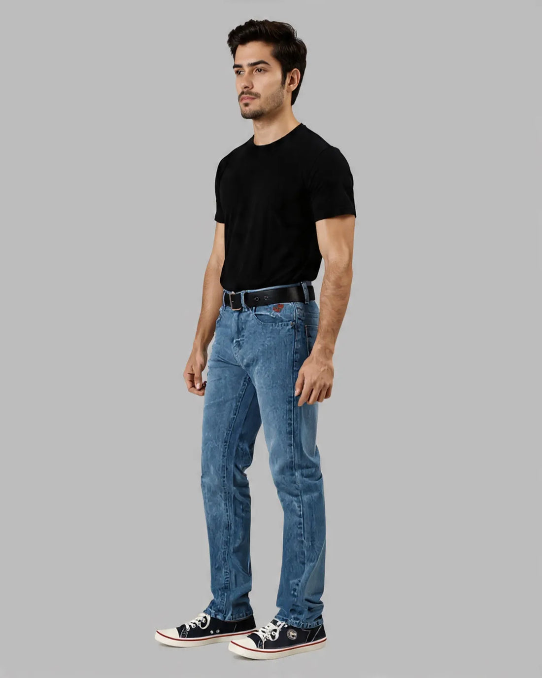 Man wearing a black t-shirt with a red logo and blue jeans on a gray background