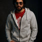 Man wearing a gray hoodie over a red shirt with sunglasses on a dark background